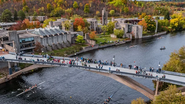 Aerial view of Trent’s Peterborough campus, with a pedestrian bridge across the river and autumn trees